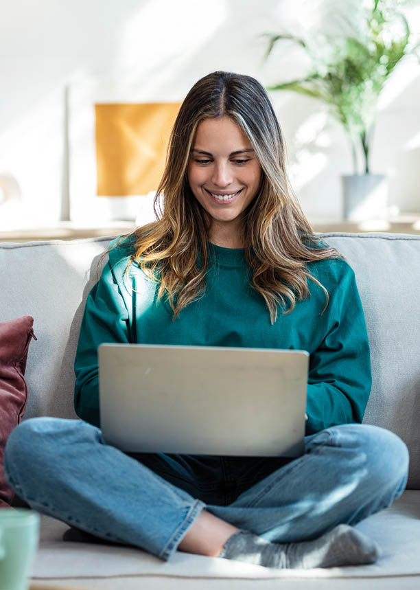 Shot of beautiful kind woman working with laptop while sitting on couch in living room at home