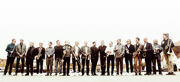 Die SWR 3 Big Band steht nebeneinander in einer Reihe. Die Blasmusiker halten dabei ihre Instrumente in der Hand.