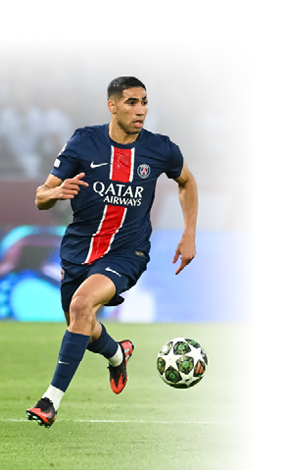 Der Fu ballspieler Achraf Hakimi von Paris Saint-Germain ist in Aktion auf dem Spielfeld zu sehen. Er tr gt das dunkelblaue Trikot seines Vereins. Er l uft mit dem Ball am Fu  ber den Rasen, sein Blick ist fokussiert und sucht die n chste Anspielstation. Im Hintergrund ist der Fu ballplatz leicht verschwommen zu erkennen.