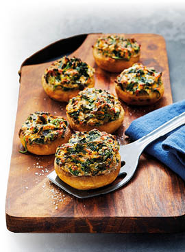 Auf einem Holzbrett sind sechs gef llte Riesenchampignons zu sehen. Die Pilze sind goldbraun berbacken.
