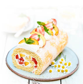 Biskuitrolle aus hellem Teig liegt auf einem hellblauen Teller. Die Rolle ist mit einer hellen Creme sowie mit Erdbeer- und Pfirsisch-St ckchen gef llt. Obenauf ist die Rolle mit Pfirsichscheiben, Erbeerh lften, Minzbl ttern und Sahne dekoriert. Neben der Rolle liegen kleine G nsebl mchen auf dem Teller.