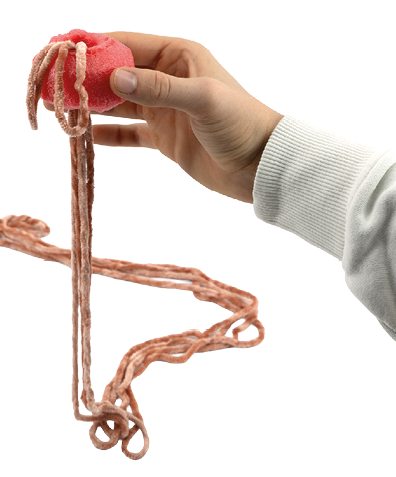 Auf dem Bild ist eine Hand zu sehen, die ein St ck Poolnudel h lt, rot und schwammartigen. Aus diesem Objekt h ngen mehrere lange, orangene Wollf den herab. Die Person tr gt einen hellen, lang rmeligen Pullover.