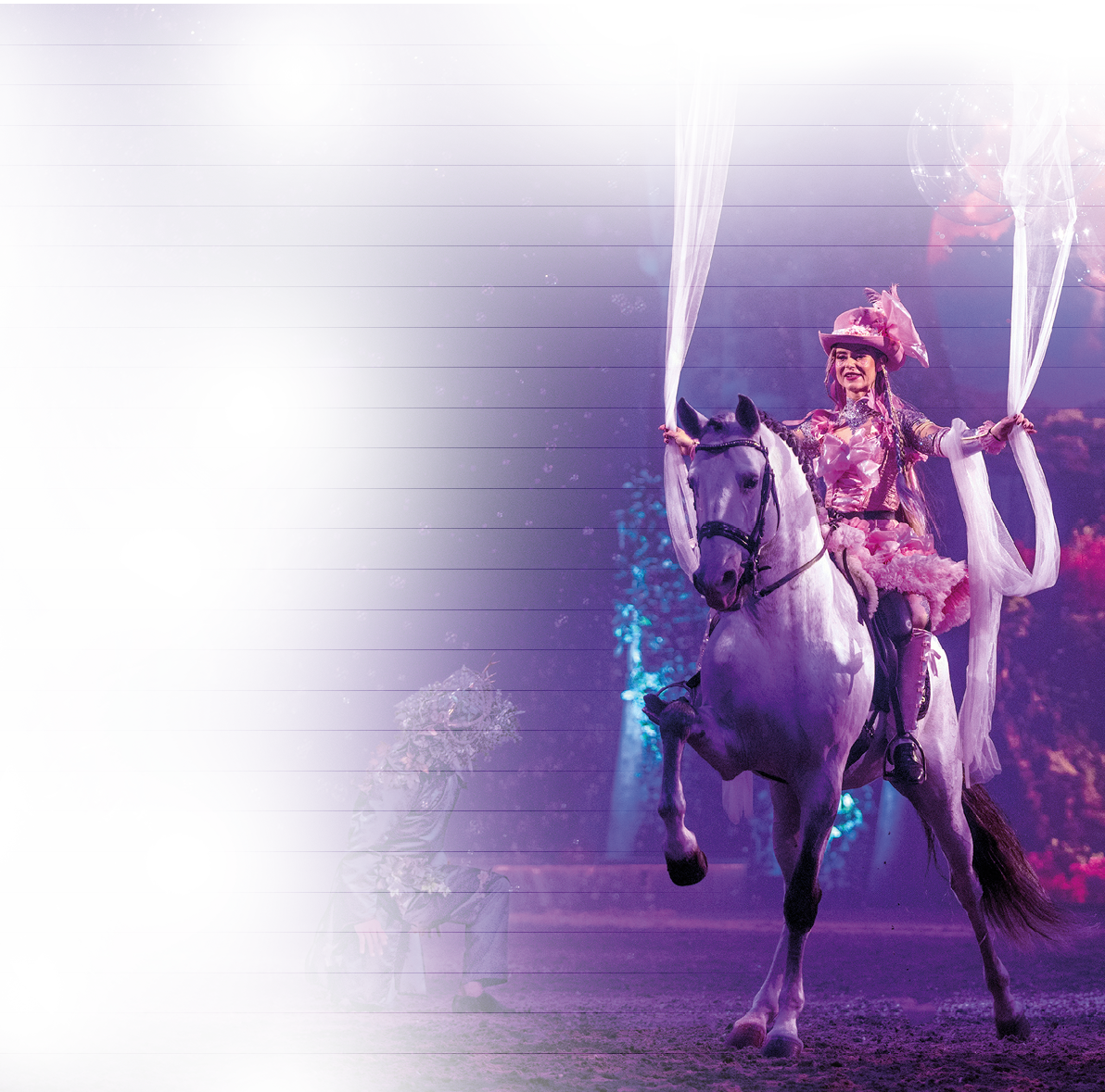 In leuchtenden Farben und m rchenhafter Kulisse reitet eine Darstellerin in einem pr chtigen pinkfarbenen Kost m auf einem wei en Pferd durch die Manege. ber ihr schwingen zarte Stoffbahnen, die der Szene eine fast schwerelose Eleganz verleihen. Das Lichtspiel aus Violett und Blau taucht die Szenerie in magischen Glanz, w hrend das Pferd stolz und anmutig auftritt. Ein Moment voller Fantasie und Zauber – wie aus einem Traum entsprungen.