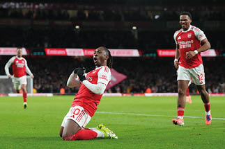 Fu ballspieler in rot-wei er Arsenal-Trikotfarbe kniet auf dem Spielfeld und feiert, zwei weitere Spieler im Hintergrund.