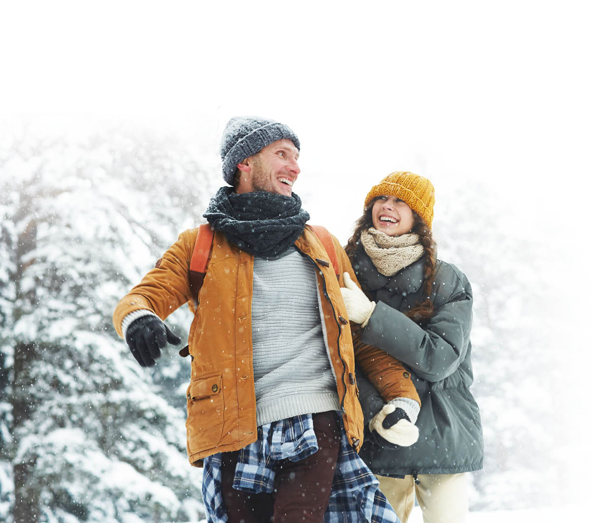 Jolly beautiful young couple in puffy jackets holding hands and laughing while enjoying winter stroll, hiking in forest