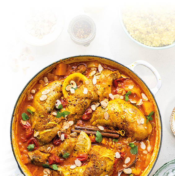 Topf mit H hnchenschenkeln in Tomatensauce, garniert mit Mandelbl ttchen, Zitronenscheiben, Zimtstangen und frischen Kr utern