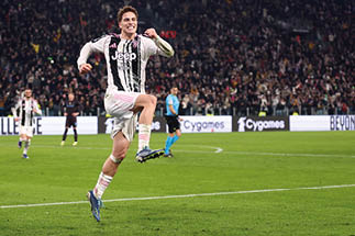 Mann in schwarzem Mantel mit erhobenen H nden vor unscharfem Hintergrund mit Menschen und rotem Banner