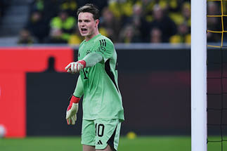 Zwei Fu ballspieler in gr nen Trikots mit Volkswagen-Logo, einer tr gt ein Regenbogenarmband am linken Arm, im Hintergrund Zuschauer im Stadion