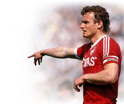 Auf dem Bild ist ein ehemaliger Fu ballspieler zu sehen, der ein rotes Trikot tr gt. Es handelt sich um Hans-Peter Briegel, genannt „Die Walz von der Pfalz“. Er war ein bekannter deutscher Spieler. Briegel zeigt mit dem rechten Arm zur Seite – vermutlich w hrend eines Spiels. Das Foto wirkt historisch, aus den 1980er Jahren.