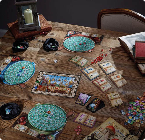 Auf einem rustikalen Holztisch ist ein Brettspiel vollst ndig aufgebaut. Drei gro e, runde Spielertableaus mit gr nem, spiralf rmigem Muster liegen verteilt auf dem Tisch; darauf befinden sich farbige Spielsteine bzw. Marker. In der Tischmitte liegt ein rechteckiges Spielbrett mit einer bebilderten Leiste und vielen kleinen Feldern am Rand. Rechts daneben sind mehrere Kartenstapel und offen ausliegende Karten zu sehen, jeweils mit Symbolen und farbigen Markierungen. Mehrere kleine Spielmaterialien liegen verstreut: rote Marker, durchsichtige und bunte Chips sowie kleine Beutel oder Schalen mit weiteren Teilen. Oben links steht eine dunkle Laterne mit einer Kerze, rechts oben liegt ein aufgeschlagenes Buch oder Heft; insgesamt wirkt die Szene wie eine stimmungsvolle, abendliche Spielrunde.