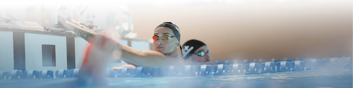Zwei Personen schwimmen in einem Hallenbad nebeneinander in Bahnen, eine davon tr gt Schwimmbrille und Badekappe. Beschreibung von KI generiert