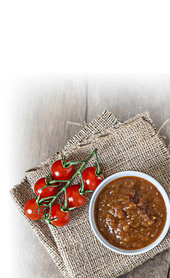 Eine Schale mit brauner Sauce liegt auf einem grob gewebten Stoff, daneben ein Zweig mit roten Kirschtomaten auf einer h lzernen Oberfl che. Beschreibung von KI generiert