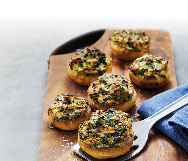 Gef llte Champignons mit Kr utern und K se auf einem Holzbrett mit einem blauen Tuch und einem Metallheber. Beschreibung von KI generiert