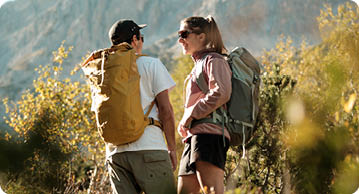 Zwei Personen mit Rucks cken unterhalten sich beim Wandern in einer bergigen Landschaft bei sonnigem Wetter. Beschreibung von KI generiert