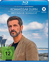 Ein Erwachsener mit kurzem dunklem Haar und Bart tr gt eine braune Jacke und steht vor einer K stenlandschaft mit einem Haus und blauem Himmel im Hintergrund, auf dem Blu-ray-Cover von Kommissar Dupin Bretonische Sehnsucht. Beschreibung von KI generiert