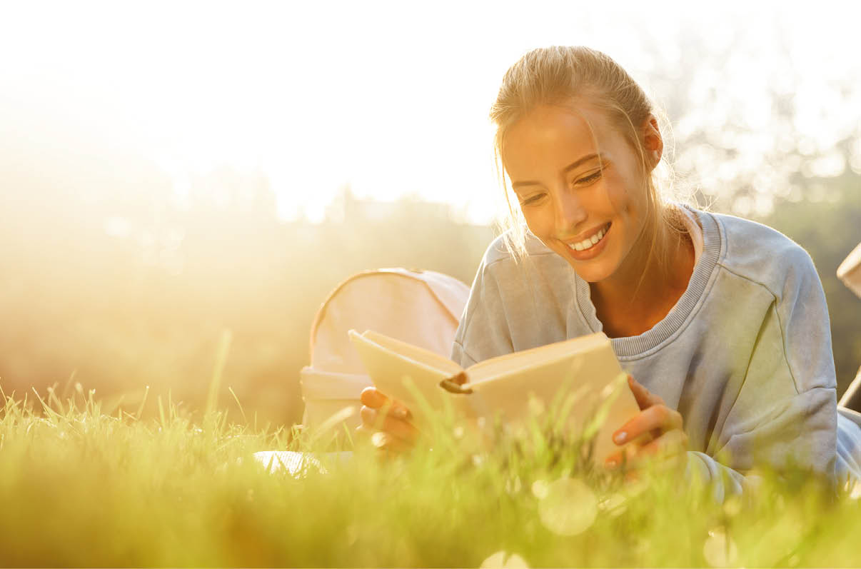 Eine Person liegt auf einer Wiese im Sonnenlicht und liest ein Buch, w hrend sie entspannt die Beine anhebt. Beschreibung von KI generiert