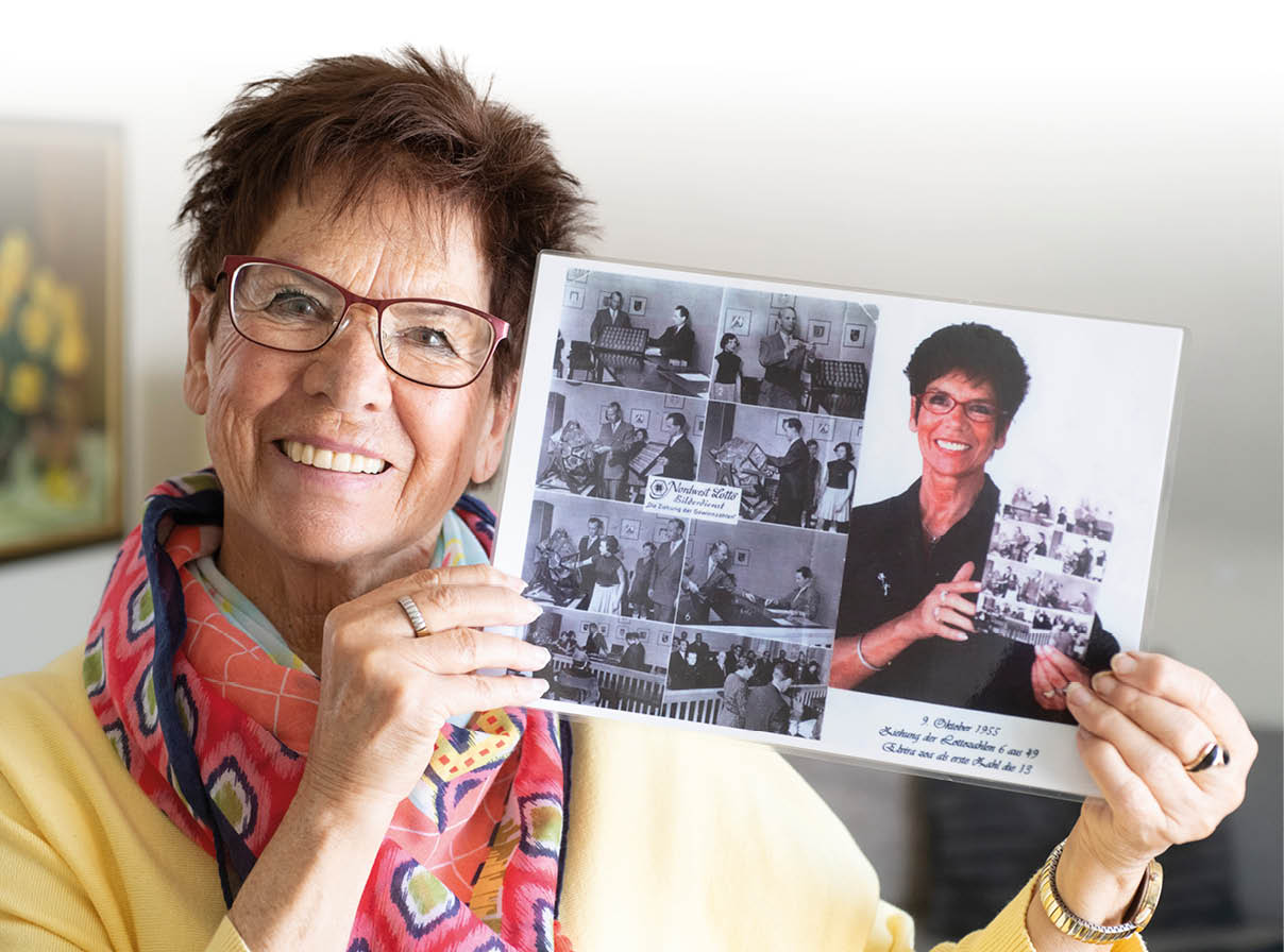 Eine l chelnde Person mit kurzen Haaren, Brille und buntem Schal h lt eine Fotocollage mit mehreren Schwarz-Wei -Bildern und einem farbigen Portr tfoto. Beschreibung von KI generiert