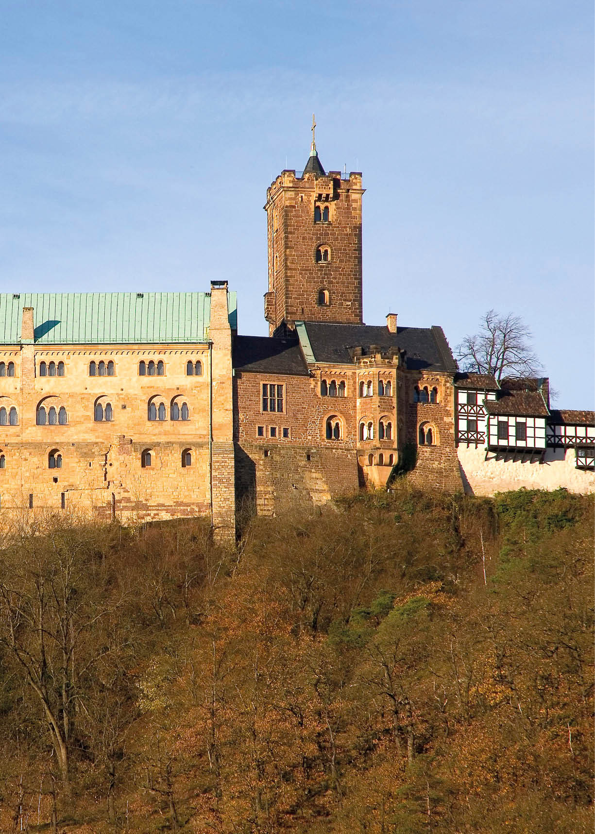 Eine gro e historische Burg mit mehreren T rmen steht auf einem bewaldeten H gel unter klarem blauem Himmel. Beschreibung von KI generiert