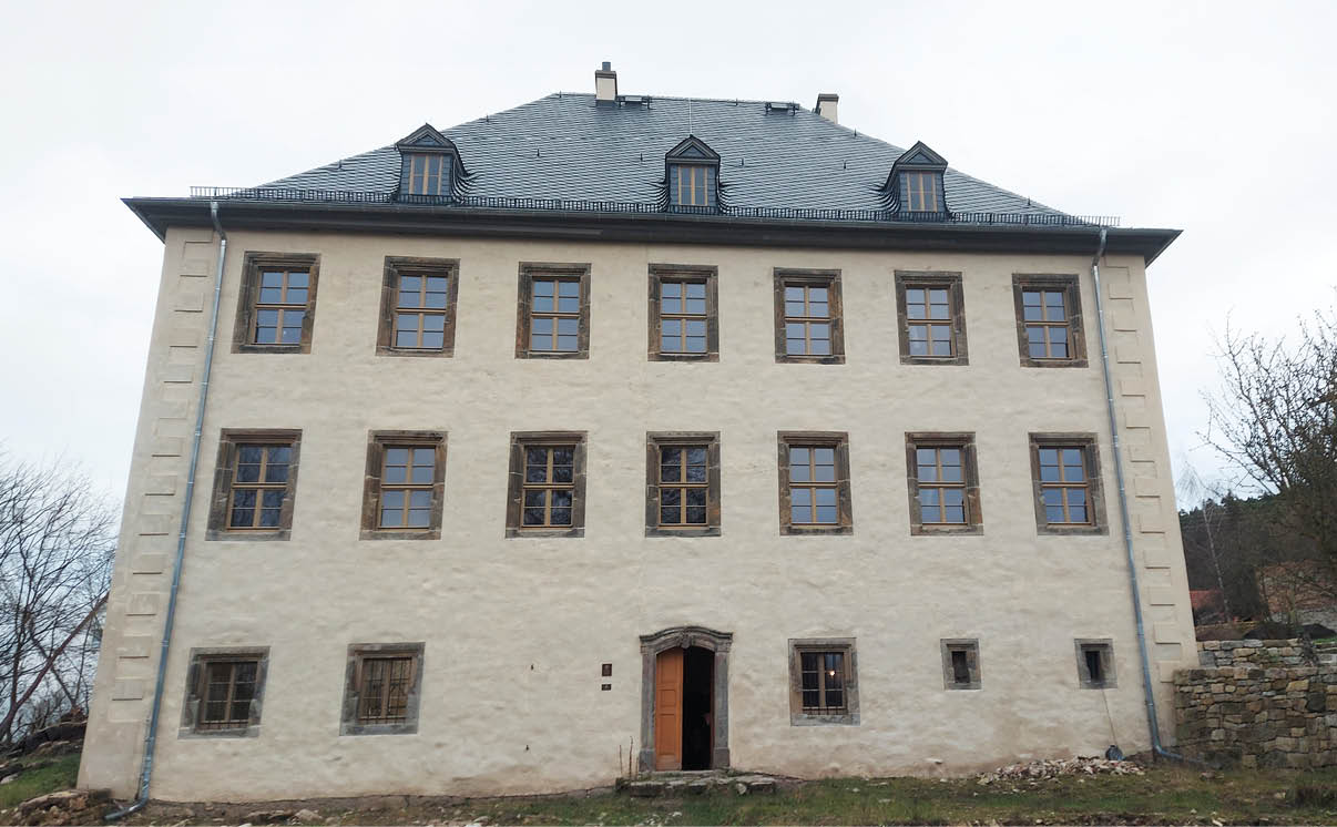 Ein gro es, historisches Geb ude mit mehreren symmetrisch angeordneten Fenstern und einem steinernen Dach bei bew lktem Himmel. Beschreibung von KI generiert