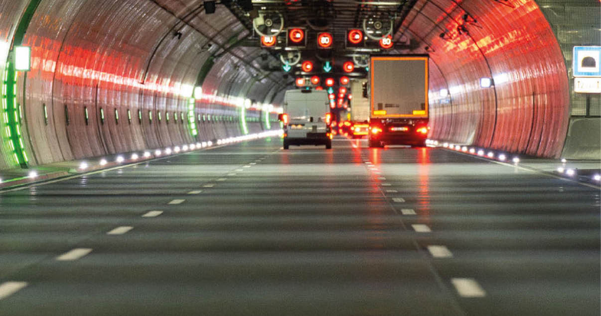 Ein mehrspuriger Tunnel mit Fahrzeugen, beleuchtet von roten und gr nen Lichtern sowie Verkehrsschildern mit Pfeilen und Geschwindigkeitsbegrenzungen. Beschreibung von KI generiert