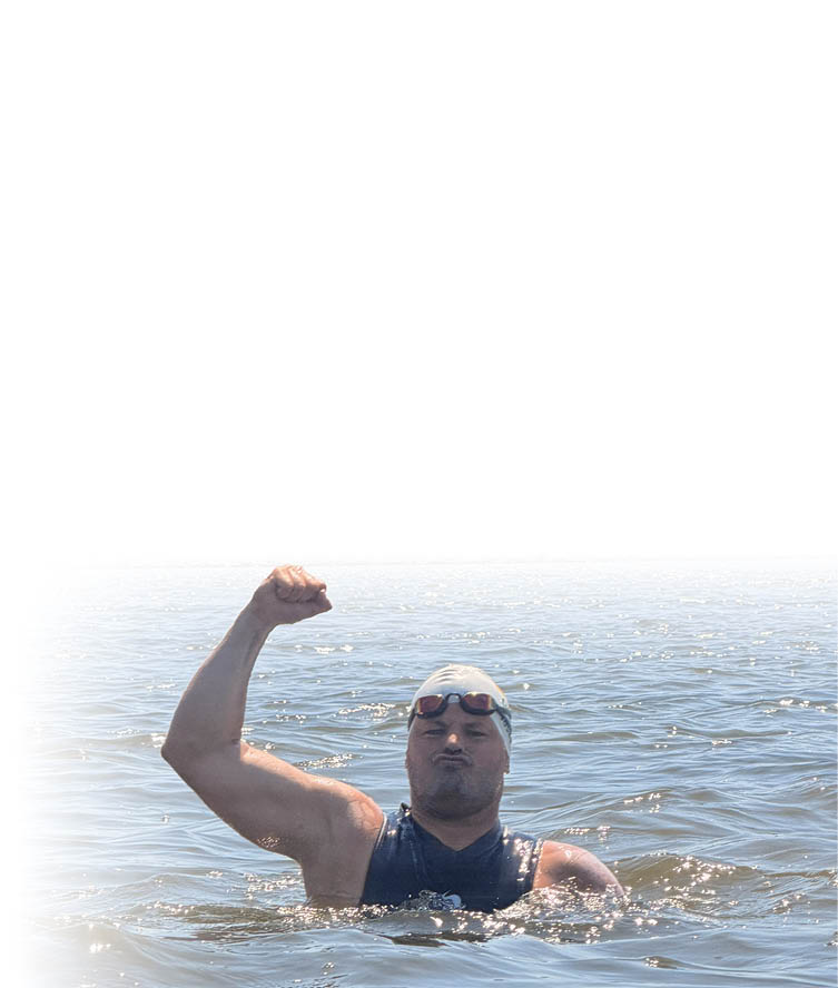Eine Person mit Schwimmkappe und Schwimmbrille zeigt im Wasser eine siegesbewusste Faust. Beschreibung von KI generiert
