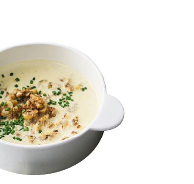 Eine wei e Sch ssel mit cremiger Suppe, garniert mit gehackten N ssen und frischen Kr utern. Beschreibung von KI generiert