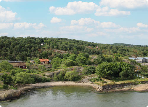 Eine ruhige K stenlandschaft mit Felsen, B umen, mehreren kleinen H usern und einem bew lkten Himmel. Beschreibung von KI generiert