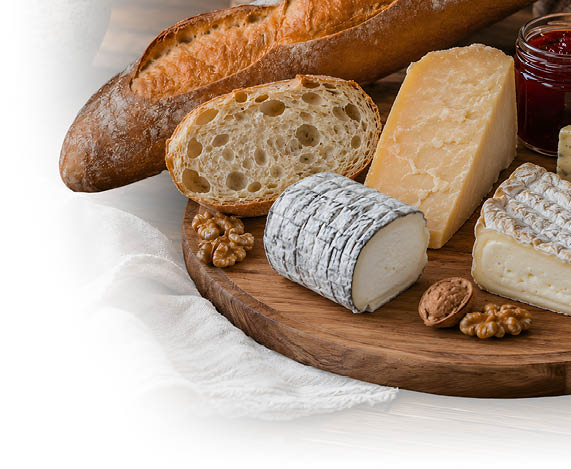 Verschiedene K sesorten, Baguette, Waln sse und ein Glas Marmelade sind auf einem runden Holzbrett auf einem Holztisch angerichtet. Beschreibung von KI generiert