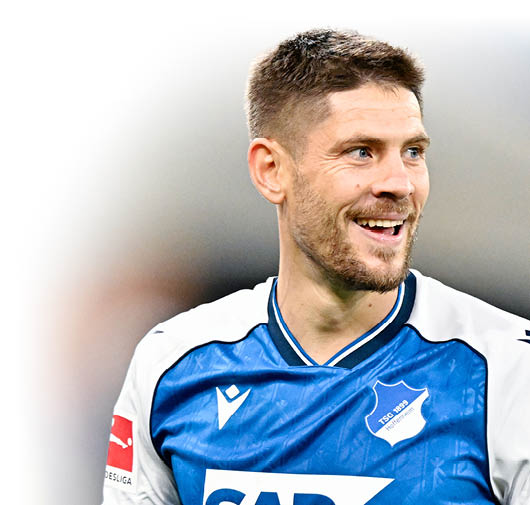 Eine Person mit kurzem Haar tr gt ein blau-wei es Fu balltrikot und l chelt w hrend eines Spiels. Beschreibung von KI generiert